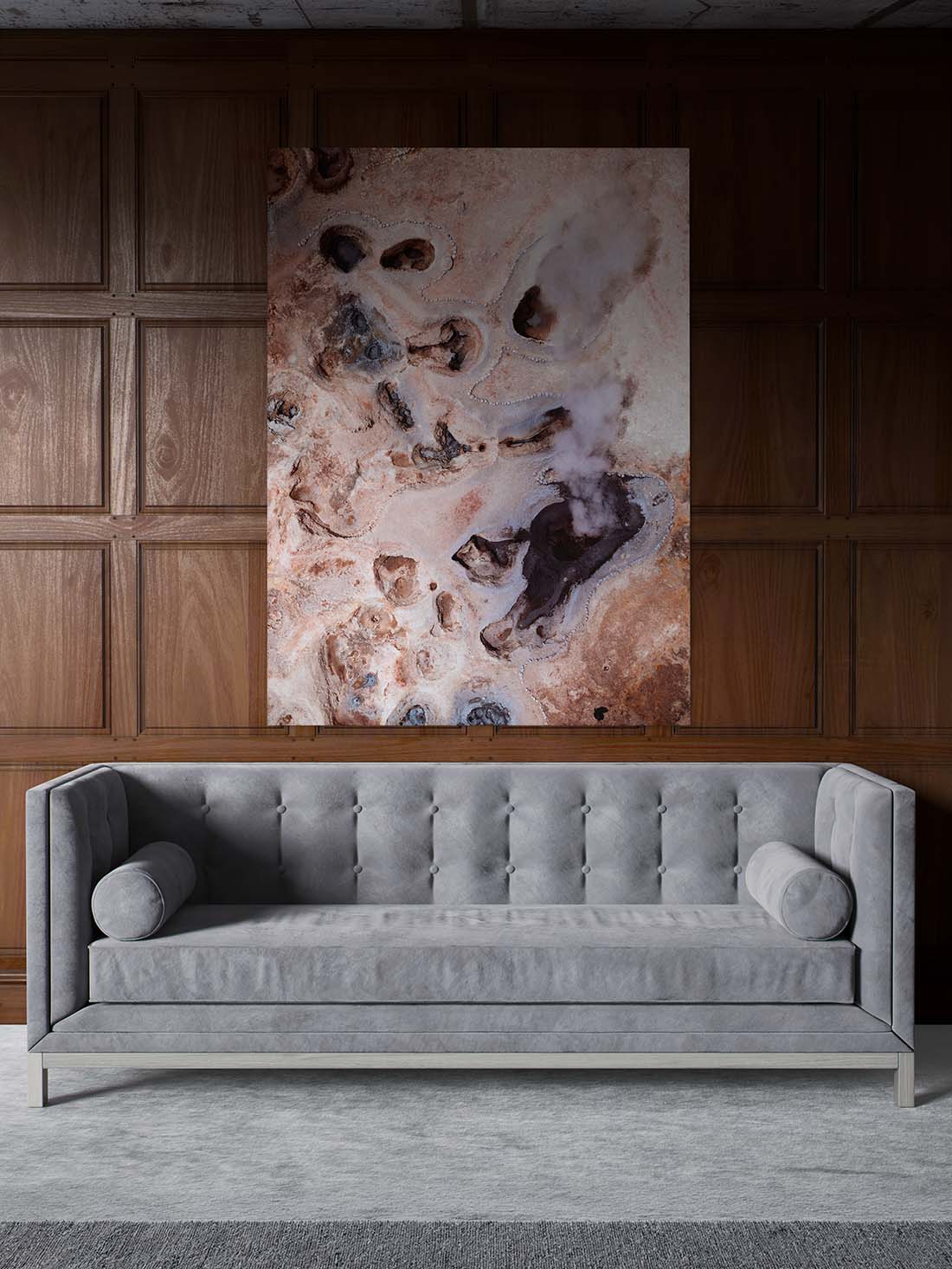 Großformatiges Wandbild in warmen Erdtönen als zentrales Element der Raumgestaltung über einem grauen Sofa vor dunkler Holzvertäfelung.